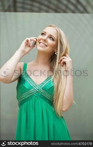 Young beautiful blonde woman in the green dress talking on cell phone, indoor