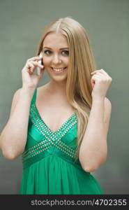 Young beautiful blonde woman in the green dress talking on cell phone, indoor