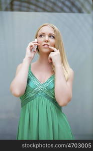 Young beautiful blonde woman in the green dress talking on cell phone, indoor