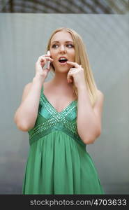 Young beautiful blonde woman in the green dress talking on cell phone, indoor