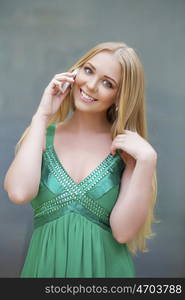 Young beautiful blonde woman in the green dress talking on cell phone, indoor