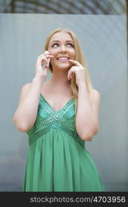 Young beautiful blonde woman in the green dress talking on cell phone, indoor