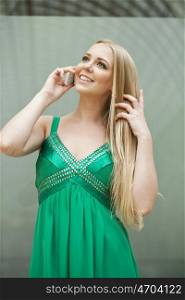 Young beautiful blonde woman in the green dress talking on cell phone, indoor