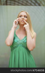 Young beautiful blonde woman in the green dress talking on cell phone, indoor