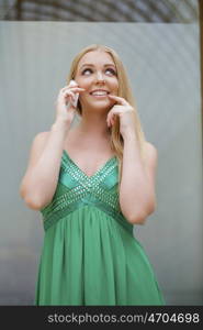 Young beautiful blonde woman in the green dress talking on cell phone, indoor