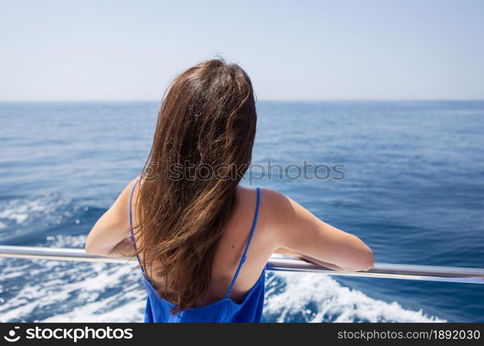 Young beautiful brunette girl sits with her back on a yacht against the backdrop of a beautiful blue sea or ocean. Young beautiful brunette girl sits with her back on a yacht against the backdrop of a beautiful blue sea or ocean.