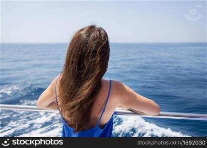 Young beautiful brunette girl sits with her back on a yacht against the backdrop of a beautiful blue sea or ocean. Young beautiful brunette girl sits with her back on a yacht against the backdrop of a beautiful blue sea or ocean.