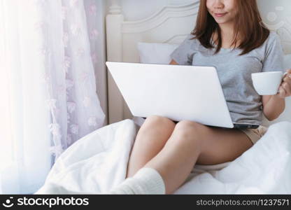 Young beautiful brunette hair woman using computer laptop and drinking coffee while sitting on the bed in the morning. close up.