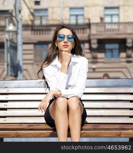 Young beautiful business woman sitting on a bench in the sunny city