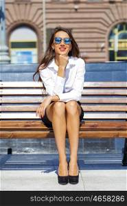 Young beautiful business woman sitting on a bench in the sunny city