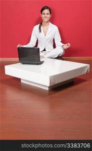 Young beautiful businesswoman sitting in yoga lotus position with laptop on table