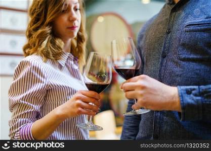 Young beautiful caucasian girl woman toasting to unknown man while standing and holding a glasses of red wine selective focus at home or winery