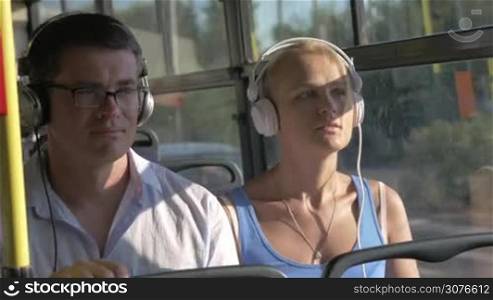 Young beautiful couple blond woman and man in glasses listening music in headset during bus trip against bus windows view
