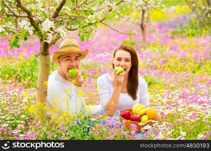Young beautiful couple having picnic outdoors in summer time, biting fresh green apple, relaxation outdoors, love concept