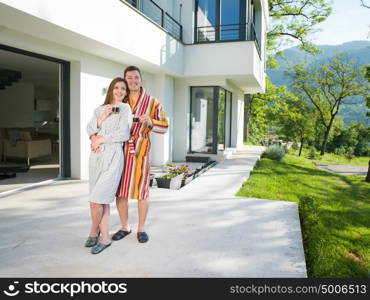 Young beautiful couple in bathrobes are enjoying morning coffee in front of their luxury home villa