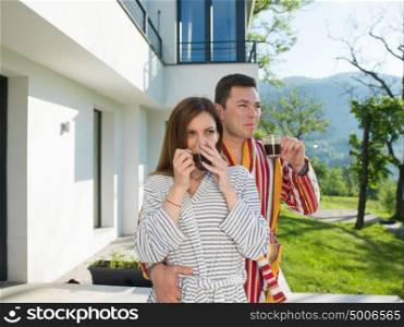 Young beautiful couple in bathrobes are enjoying morning coffee in front of their luxury home villa