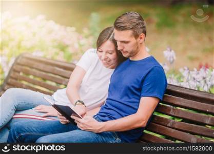 Young beautiful couple on a bench in the park reading together. Relaxed young family on the bench in the park
