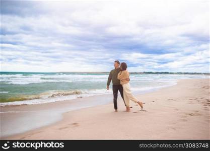 Young beautiful couple on the beach in windy and cloudy weather. Young family on the beach in the storm