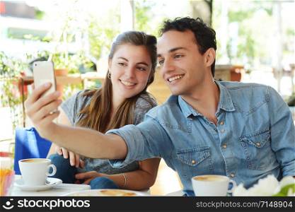 Young beautiful couple taking a selfie with smartphone in coffee shop.