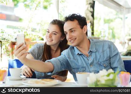 Young beautiful couple taking a selfie with smartphone in coffee shop.