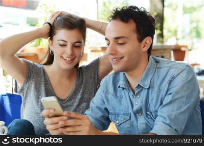 Young beautiful couple using smartphone in coffee shop.