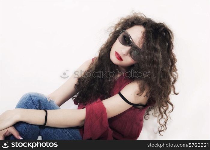 Young beautiful curly brunette woman in sunglasses on light background