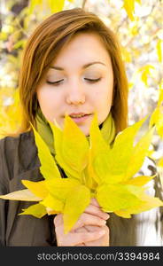 young beautiful european girl looks at bunch of autumn leaves in her hands