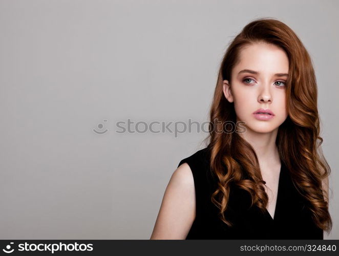 Young beautiful fashion model wearing black dress with no sleeves on grey background using hard light