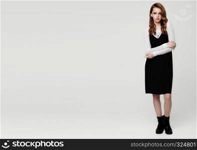 Young beautiful fashion model wearing black dress with white shirt on grey background