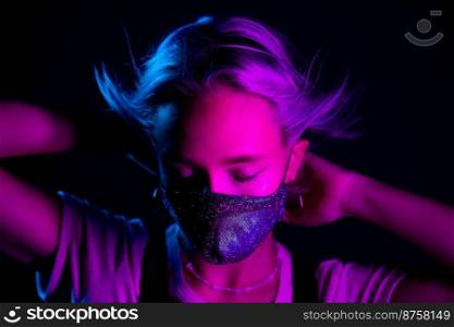 Young beautiful fashionable woman in protective mask with rhinestones dancing in night club. Neon colorful light. Close-up portrait of fashion model. Young beautiful fashionable woman in protective mask with rhinestones dancing in night club. Neon colorful light. Close-up portrait of fashion model.