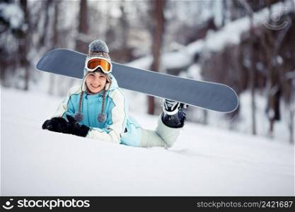Young beautiful female snowboarder resting on ski slope, she’s lying on stomach and smiling