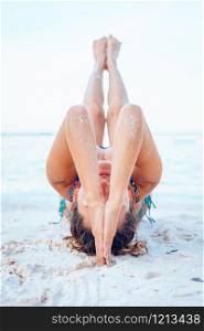 Young beautiful fit caucasian woman in summer girl bikini swimsuit practice yoga at the beach by the sea or ocean in sunny day stretching on the vacation