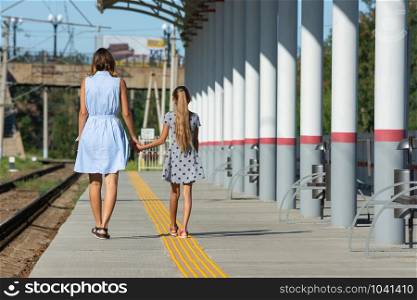 Young beautiful girl and teenage daughter walk from the camera on the empty platform of the train station