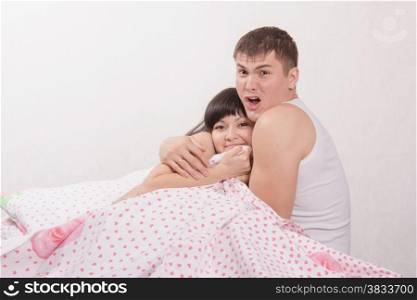 Young beautiful girl and the guy sitting in bed cuddling