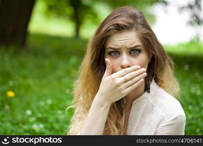 Young beautiful girl covers her mouth with his hand, posing outdoors in summer park