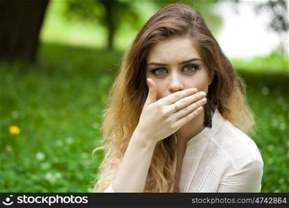 Young beautiful girl covers her mouth with his hand, posing outdoors in summer park