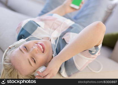 Young beautiful girl enjoying music through headphones, laying on sofa at home