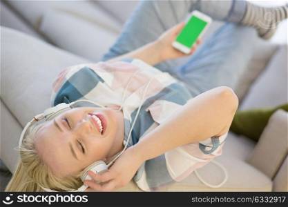 Young beautiful girl enjoying music through headphones, laying on sofa at home