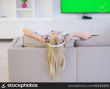 Young beautiful girl enjoying music through headphones, laying on sofa at home