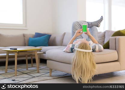 Young beautiful girl enjoying music through headphones, laying on sofa at home