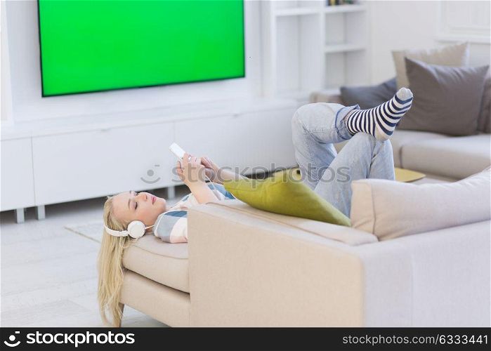 Young beautiful girl enjoying music through headphones, laying on sofa at home