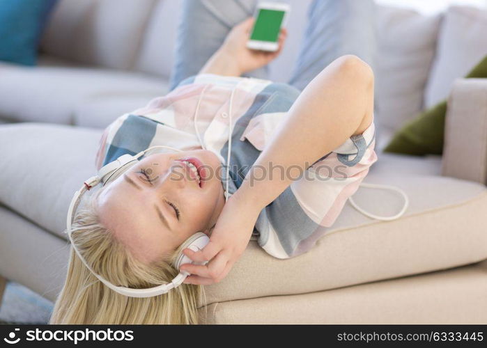 Young beautiful girl enjoying music through headphones, laying on sofa at home