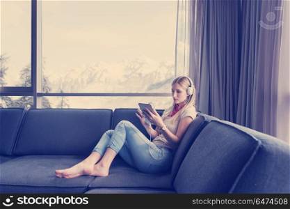Young beautiful girl enjoying music through headphones, laying on sofa near the window at home. young girl enjoying music through headphones