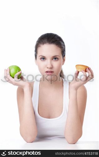Young beautiful girl holding a green apple and cake on a white background
