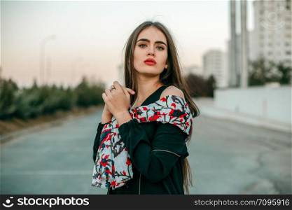 Young beautiful girl in a black jacket with a scarf posing in the evening on the street.