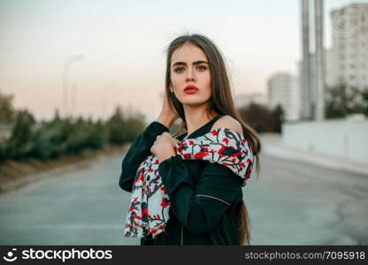 Young beautiful girl in a black jacket with a scarf posing in the evening on the street.