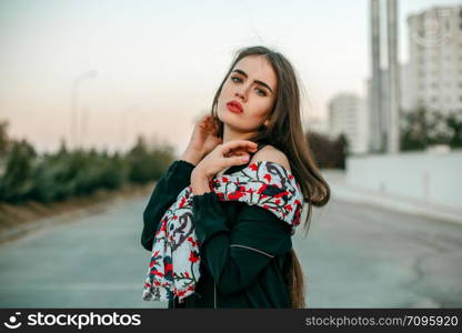 Young beautiful girl in a black jacket with a scarf posing in the evening on the street.