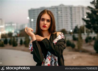 Young beautiful girl in a black jacket with a scarf posing in the evening on the street.
