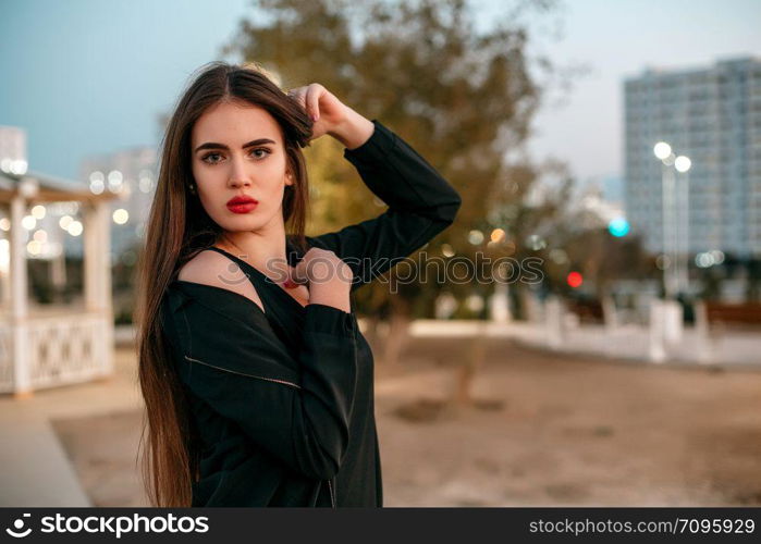 Young beautiful girl in a black jacket with a scarf posing in the evening on the street.