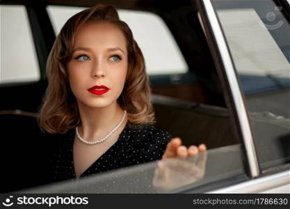 young beautiful girl in a black vintage polka dot dress sitting in a vintage white car.